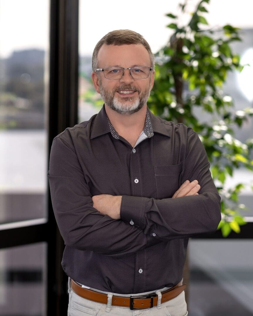 A man with his arms crossed standing in front of a window.