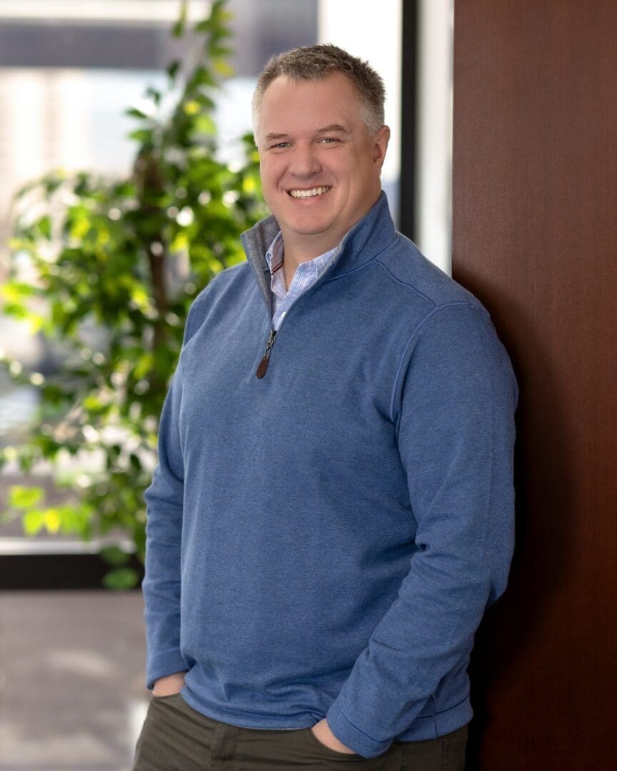 A man standing in front of a wall with his hands in pockets.