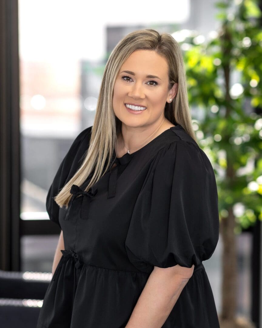A woman in black dress standing next to a tree.