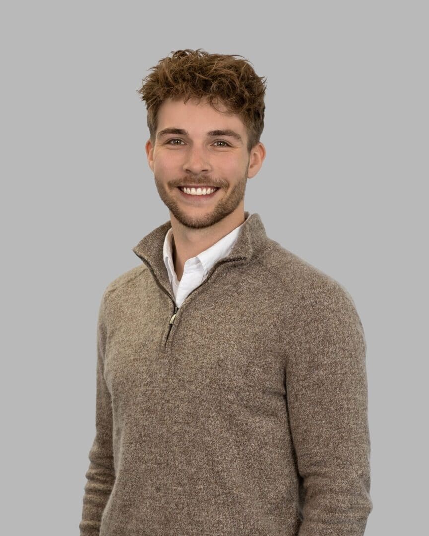 A man in brown sweater standing next to wall.